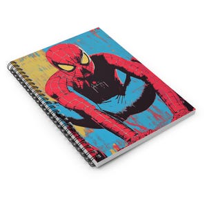 May include: A spiral-bound notebook featuring a graphic illustration of a red and blue costumed superhero in a crouching pose. The cover art displays a stylized comic book aesthetic with bold lines, yellow eyes, and a black spider emblem on the chest.