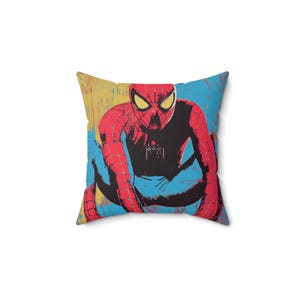May include: A red and blue throw pillow with a graphic of Spiderman in a crouching pose on a yellow, blue, and black background.