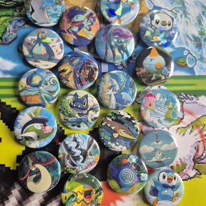 Peut inclure: Une collection de boutons ronds et colorés représentant divers personnages de dessins animés. Les boutons ont une finition brillante et sont principalement bleus, verts et jaunes. Les personnages sont placés sur un fond de carte.