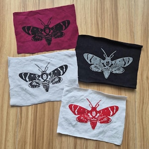 May include: Four fabric patches with a black and white moth design. The moths are printed on white, red, and black fabric. The moths have a skull and crossbones design on their bodies.
