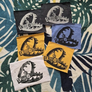 May include: Six fabric patches featuring a black and white print of a bear trap. The patches are in a variety of colours, including yellow, blue, and white.