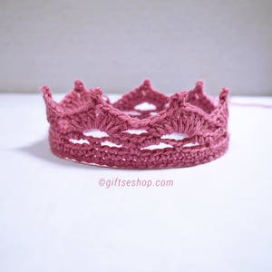 May include: A pink crocheted crown with a delicate openwork design. The crown is made with a soft yarn and has a delicate, feminine look.