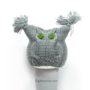 May include: Grey knitted owl hat with green felt eyes and two long grey yarn tassels on top.