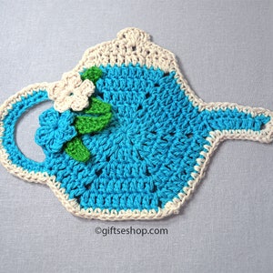 May include: A crocheted teapot hot pad in teal blue with a white crocheted border. The hot pad has a white crocheted flower with green leaves.