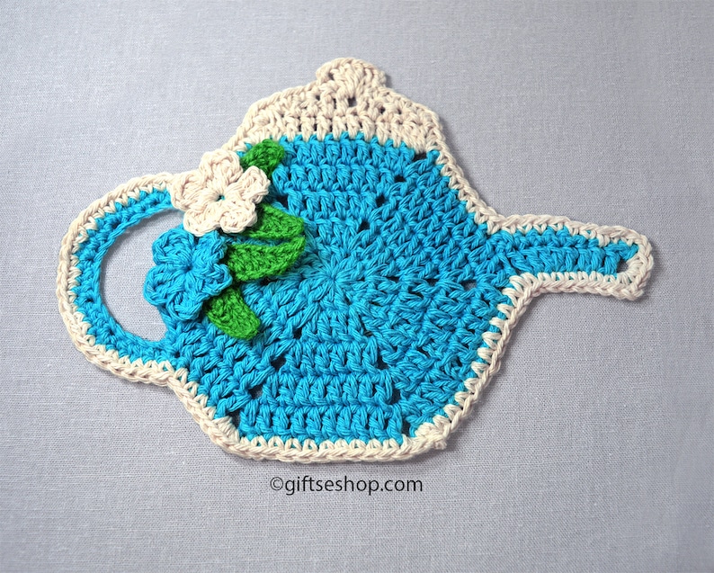 May include: A crocheted teapot hot pad in teal blue with a white crocheted border. The hot pad has a white crocheted flower with green leaves.