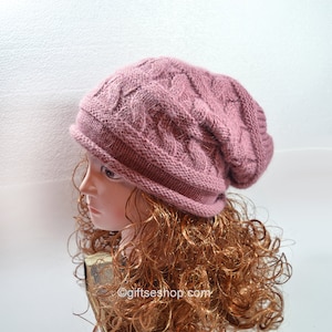 May include: A pink knitted beanie with a cable knit pattern. The beanie is slouchy and has a fold-over brim.