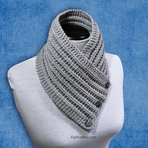May include: A grey knitted cowl neck scarf with a button closure. The scarf is folded over and has a diagonal stitch pattern.