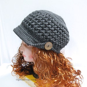 May include: A gray crocheted newsboy cap with a button on the side. The cap is on a mannequin with long, curly red hair.