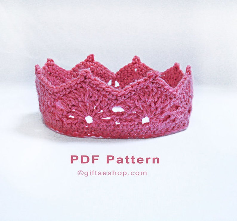 Op de afbeelding: Een roze gehaakte kroon met een gegolfde rand. De kroon is gemaakt met een delicaat steekpatroon en heeft een licht verhoogd midden. De kroon staat op een witte achtergrond. PDF-patroon &copy;giftseshop.com
