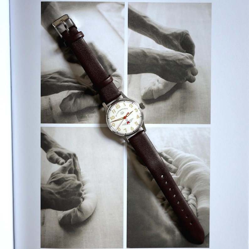 May include: A wristwatch with a silver case and a cream face, featuring black numerals and red details. It has a brown leather strap. The watch is displayed against a backdrop of black and white images.