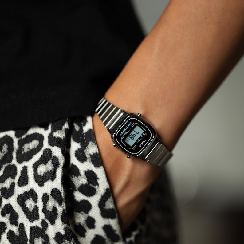 K&ouml;nnte beinhalten: Eine silberfarbene Digitalarmbanduhr mit einem Metallgliederarmband und einem rechteckigen schwarzen Zifferblatt. Die Uhr verf&uuml;gt &uuml;ber eine Digitalanzeige mit Uhrzeit sowie den Markennamen Casio und den Schriftzug Water Resist.