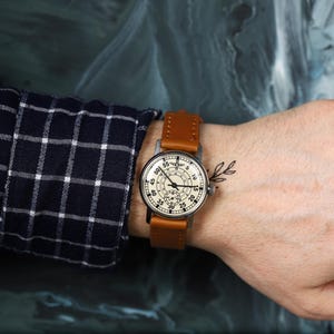 May include: A wristwatch with a white face and black markings. The watch has a brown leather band and a silver case. The watch is on a person's wrist.