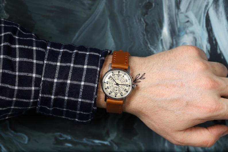 May include: A wristwatch with a white face and black markings. The watch has a brown leather band and a silver case. The watch is on a person's wrist.