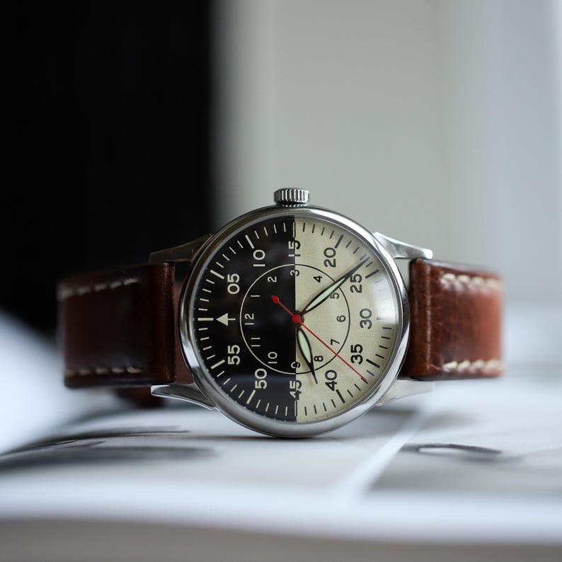 May include: A wristwatch with a two-tone black and cream face, featuring a brown leather strap. The watch has a silver-colored case and a red second hand. The face displays numbers and markers for timekeeping.