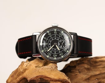 May include: A black leather watch band with red stitching, attached to a silver wristwatch with a black face and white numerals. The watch face has a small, round, white subdial.