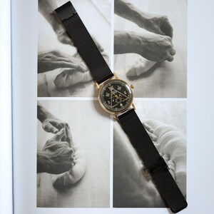 Puede incluir: Un reloj de pulsera dorado con esfera negra y correa de malla negra. La esfera del reloj presenta símbolos intrincados. El reloj se muestra en una página con fotografías en blanco y negro.