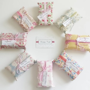 May include: Nine handmade fabric tissue boxes in various floral patterns. The boxes are tied with twine and have a small tag that reads "Handmade Fabric Tissue Box". The boxes are arranged in a circle around a white card that reads "Boutique Crafts".