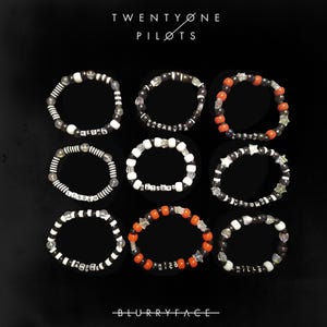 May include: Nine black and white beaded bracelets with different words on them, including "Twenty One Pilots" and "Blurryface".  The bracelets are arranged in three rows of three.