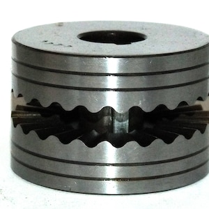 May include: A cylindrical metal object with a central hole and a wavy, gear-like design cut into the sides. The object has horizontal grooves and a dark, metallic appearance, likely made of steel.