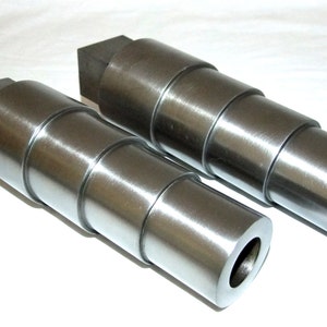 May include: Two silver metal rolling pin attachments with a square end and a round end. The attachments are made of multiple sections that can be stacked together to create different sizes of rolling pins.