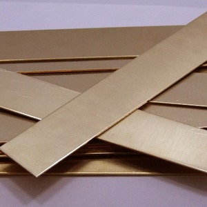 May include: A collection of rectangular brass bars, varying in size, are arranged in a slightly overlapping pattern. The bars have a polished, reflective surface, and a warm, golden hue. The arrangement suggests a craft or DIY project.