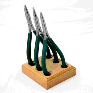 Puede incluir: Conjunto de cuatro alicates de mango verde con puntas de metal plateado, expuestos en un soporte de madera con cinco ranuras.