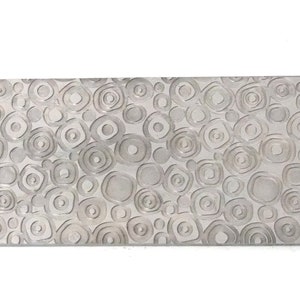 Op de afbeelding: Een zilveren metalen plaat met een getextureerd oppervlak met een herhalend patroon van cirkels en ovalen.