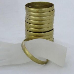 May include: A stack of gold-colored bangles, with one bangle resting on a white surface. The bangles are a simple, round design. The image is set against a white background.