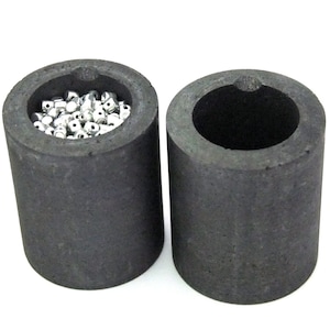 May include: Two black ceramic crucibles, one filled with silver beads, for melting metal.