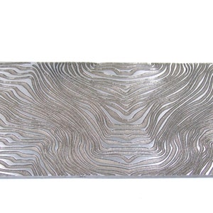 May include: A rectangular piece of metal with a unique, flowing pattern. The surface has a textured, wavy design in shades of gray and silver, resembling wood grain or water ripples. The metal piece is likely for crafting.