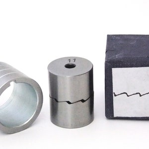 May include: Three metal parts for a machine, two are cylindrical and one is in a black box. The cylindrical parts have a silver finish and one has the number "17" engraved on it. The box has a white label with a wavy line and the number "10" written on it.