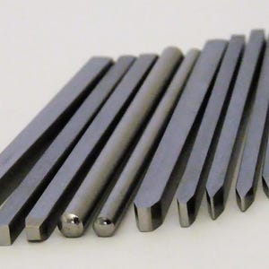 May include: A set of 15 metal tools with different shaped tips. The tools are arranged in a semi-circle, with the tips facing the viewer. The tools are all silver in color and have a smooth, polished finish.