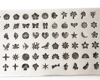 Könnte beinhalten: Ein Stempelset aus Metall mit 60 verschiedenen Designs, darunter Blumen, Herzen, Sterne, Tiere und geometrische Formen. Die Stempel sind in Reihen auf einer rechteckigen Metallplatte angeordnet.