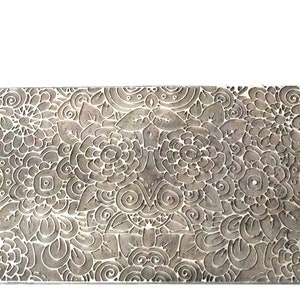 以下が含まれることがあります： 細かい花柄が刻まれた銀色の金属製のスタンプ。スタンプは長方形で、浮き彫りのデザインになっています。