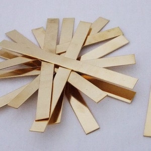 May include: A group of 15 gold-colored metal strips, arranged in a starburst pattern. One strip is separated from the group and is lying horizontally.
