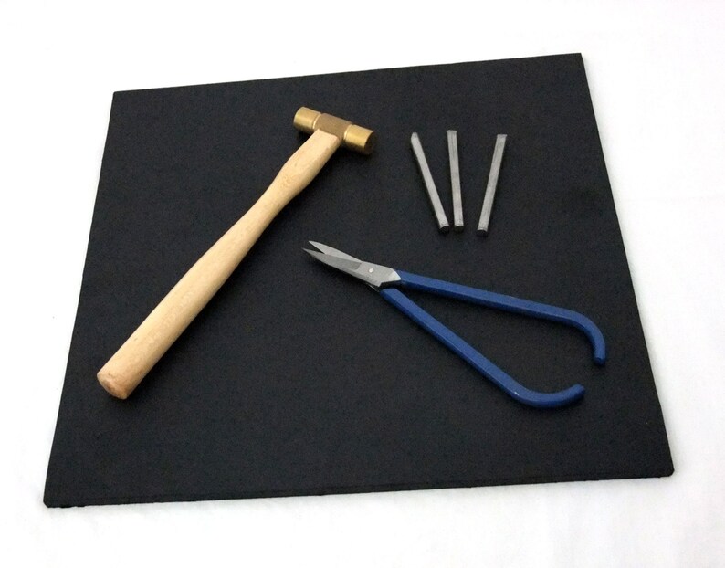Puede incluir: Una estera de goma negra con un martillo de lat&oacute;n, alicates azules y cinco varillas de metal plateado.