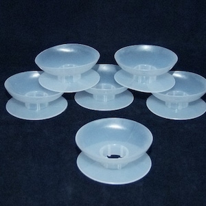 May include: Six clear plastic bobbins for a sewing machine. The bobbins are stacked on a black surface.