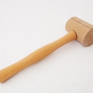 May include: A wooden meat mallet with a light brown handle and a slightly darker brown head. The head is slightly rounded and has a textured surface.