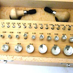 May include: A wooden box with a set of metal tools for jewelry making. The tools are organized in rows and labeled with sizes from 1.50 to 18.00. The box also includes two wooden handles with black tips.