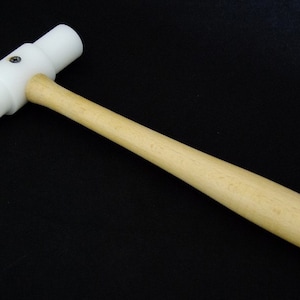 May include: A white rubber mallet with a wooden handle. The mallet has a flat head and is used for striking objects.