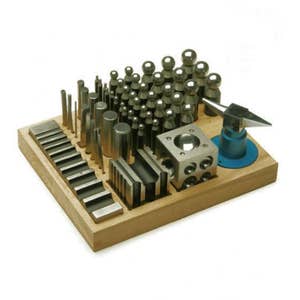 May include: A wooden jewelry-making tool set with various metal forming tools. The set includes a small anvil, a cube with holes, and a variety of metal cylinders, rods, and doming punches. The tools are arranged on a light-colored wooden base.