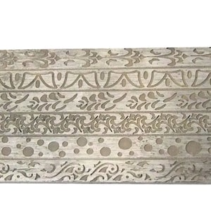May include: A silver metal sheet with a decorative pattern of repeating lines and circles. The pattern is embossed into the metal, creating a raised design.
