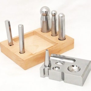 May include: A set of metal jewellery making tools with a wooden stand. The tools include a variety of round and pointed tips for shaping metal.
