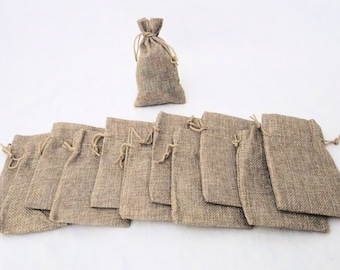 May include: A set of 11 small burlap bags with drawstrings. The bags are a light brown color and are arranged in a row. The bags are perfect for packaging small gifts or favors.