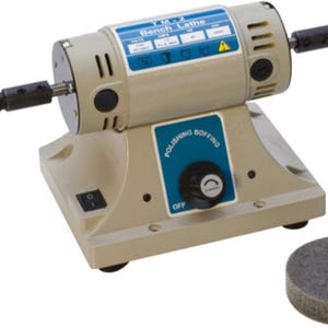 May include: A beige bench lathe with a blue and white label that reads "TM-2 Bench Lathe". It has a polishing wheel on each end and a separate polishing wheel on the base. The machine has a power switch and a dial labeled "Polishing Buffing".
