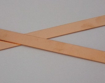 Może przedstawiać: Dwa cienkie, płaskie paski z miedzi, każdy o długości około 25 cm i szerokości 1,2 cm, leżą na białym tle, skrzyżowane ze sobą.