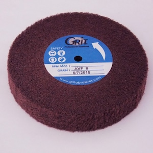 May include: A brown, round, abrasive buffing wheel with a blue label that reads "Grit Professional Abrasives" and includes safety instructions, RPM max, grain, AVF 8, and 6/7/2015. The label also includes the website www.gritabrasives.com.