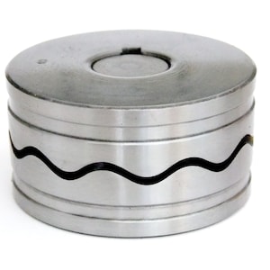 May include: A cylindrical metal object with a wavy design. The object is silver and has a circular top with a smaller circular indentation. The wavy design is a dark color and wraps around the middle of the cylinder.