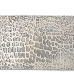 Könnte beinhalten: Nahaufnahme einer silbernen Metallplatte mit einer strukturierten Oberfläche, die einem Schlangenhautmuster ähnelt.