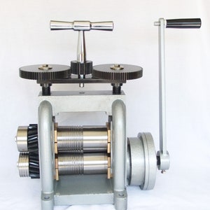 May include: A silver metal rolling mill with two sets of rollers, a hand crank, and a T-shaped handle. The rolling mill is used for shaping metal.